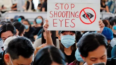 Reuters A protester in the airport holds a sign that says "stop shooting eyes"