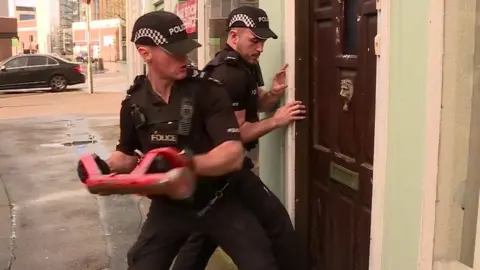 SKY/BBC Police smash down a door during a morning raid in Lancaster
