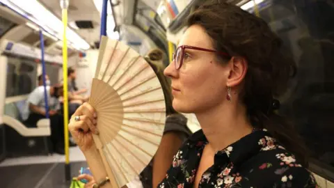 EPA A woman uses a fan to cool herself in an underground train in London