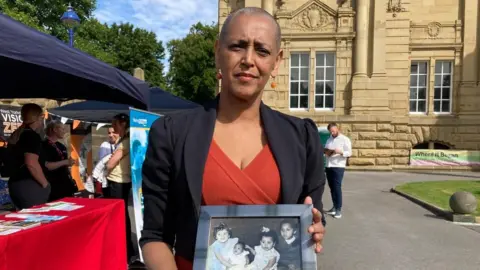 Alison Lowe holds a framed family photo of herself and her sister, who died aged three in a car collision.