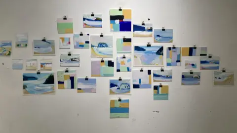 Julian Davies 33 paintings, stuck to a white wall. They use a range of blues, greens, pruples and yellows.