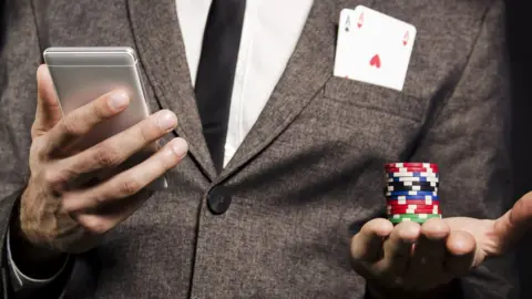 Getty Images A man in a suit holding poker chips and a smartphone