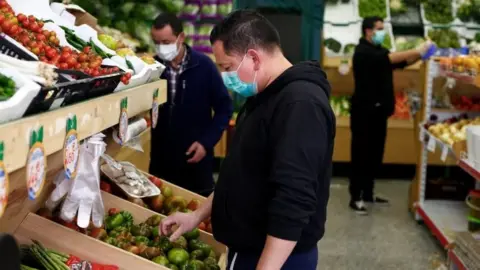 Reuters People wearing masks choose vegetables in a supermarket in Madrid, Spain. Photo: 14 March 2020