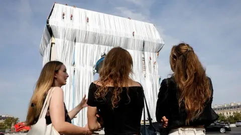 Getty Images Bystanders look on as workers arrange silver blue fabric, part of the process of wrapping the Arc de Triomphe