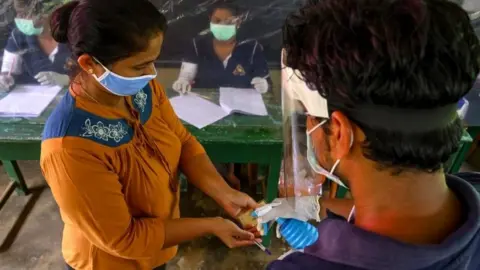 AFP An election official sprays disinfectant on a voter during a mock election in Sri Lanka, 14 June 2020