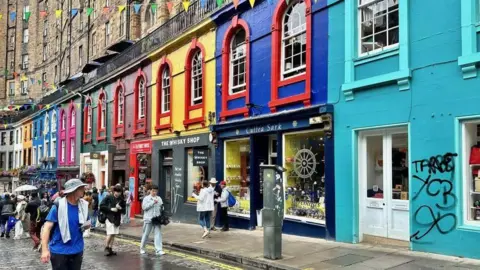 Colourful buildings painted all different colours and a cobbled road in front with tourists walking on it.