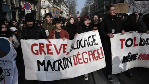 Getty Images A protester holds banner reading "Strike, blockade: Macron get out" during a demonstration in Paris on January 24, 2020