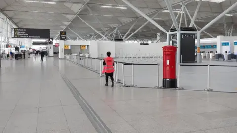 PA Media Large white terminal building, showing red pillar box, direction signs and staff member in red hi-viz jacket.