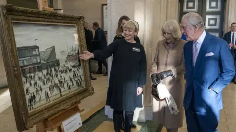 PA Media King Charles III and the Queen Consort views L.S. Lowry's "Going to the Match" painting during a visit to Bolton Town Hall