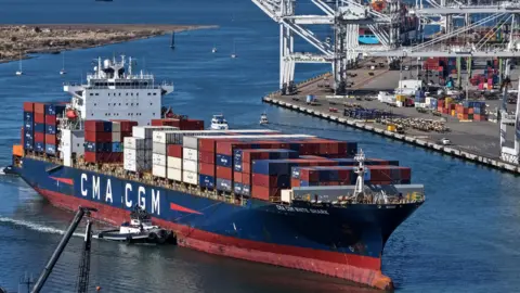 A cargo ship with the letters 'CMA CGM' comes into port with the industrial harbour in the background at the Port of Oakland in October.