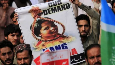 EPA A protester holds up a poster with Asia Bibi's head in a noose above a fire pit