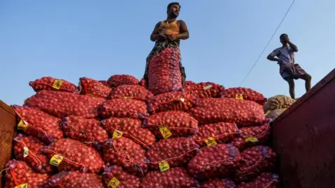 Getty Images Labourers look on as they unload bags filled with onions at a wholesale vegetable market in Chennai on February 1, 2020.