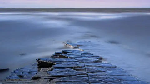 Mary Maynard long exposure dawn coastal photography of rocks emerging from water.