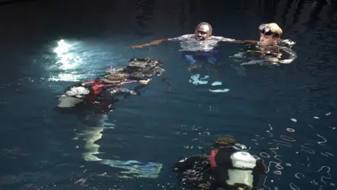 Jamie Niblock/BBC Actors and divers in a water tank