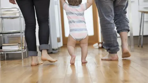 Getty Images Mum and dad holding hands with walking baby