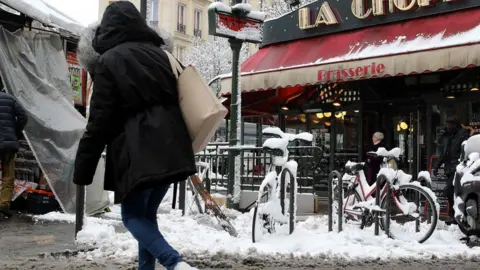 AFP/Getty Images A woman crosses a snow-covered Parisian street by a metro station entrance