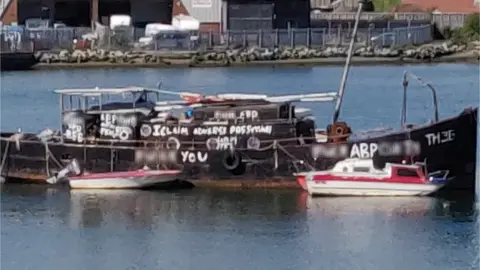 BBC A black boat daubed with swear words painted in white graffiti