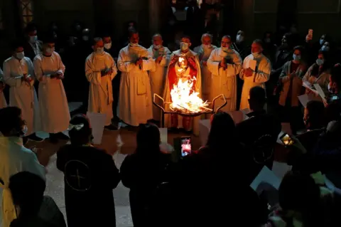 Reuters People gathered around a fire during a Mass in the Virgin Mary Church in Baghdad, Iraq. Photo: 24 December 2020