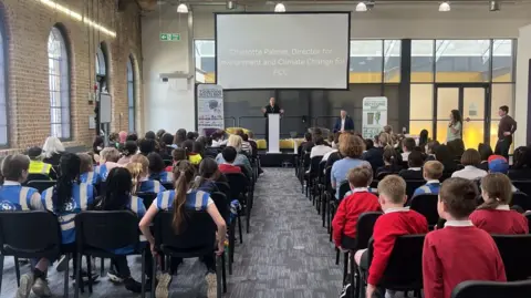School students sitting inside the council office looking at the presentation - with their backs to camera.