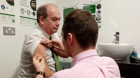 Michael McBride with shirt sleeve rolled up getting a vaccine