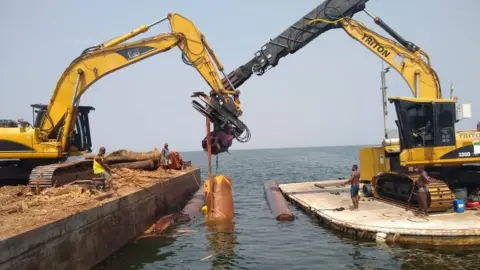 Jacob Tetteh Ageke Kete Krachi uses remotely operated machinery to extract timber from Lake Volta.