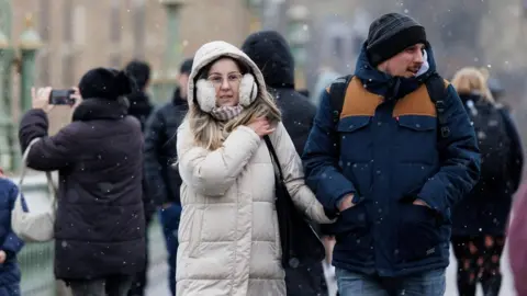 EPA People walk through a snow flurry on Westminster Bridge in London, Britain on Monday