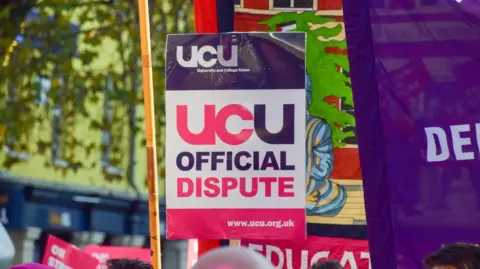 A purple, white and pink placard reading UCU official dispute, alongside a purple flag