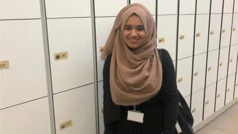 Female standing next to white lockers.