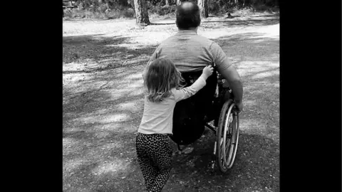  Ian Taverner Ian Taverner with one of his daughters pushing him in a wheelchair