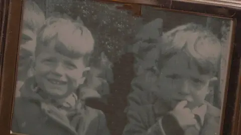 Shaun Whitmore/BBC Sepia-coloured photo of two young boys with pale coloured hair. One smiles while the other looks pensive and has a finger in his mouth.