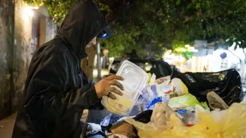 Lee Durant / BBC A person goes through litter bins in Beirut in search of recyclable plastics