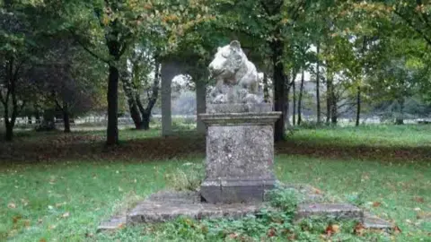 HMPC Ltd Stone statue of a lioness on a plinth, surrounded by trees, with the planned stone temple in the background