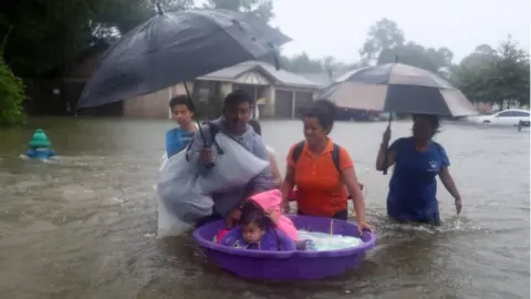 Getty Images People walk down a flooded street as they evacuate their homes after the area was inundated with flooding from Hurricane Harvey on 28 August 2017 in Houston, Texas