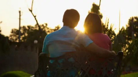 Getty Images Couple sitting on bench at sunset - stock photo