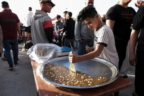 Reuters A boy cuts a piece of sweet at a popular market during the holy month of Ramadan in Benghazi, Libya. April 8, 2022. Picture taken April 8, 2022