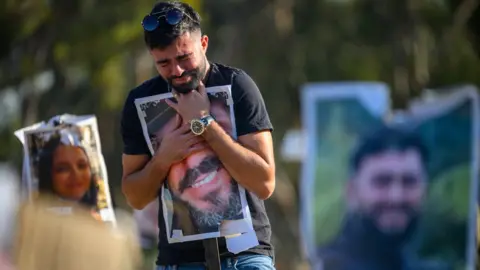 Getty Images Rudy Glazer, whose brother Ranani was killed on October 7, hugs a photo of his brother at the site of the Nova festival