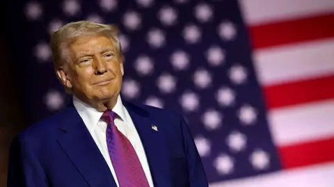 Donald Trump stands in front of the US flag