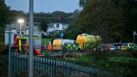 Grimsby News and Pictures A wide shot of emergency vehicles from the vantage point of a road behind the bridge.  Houses can be seen in the background.  Police tape can be seen to the right, presumably near the river.