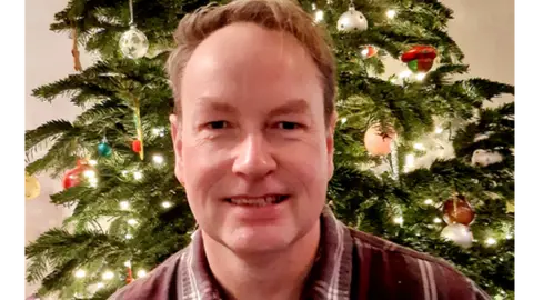 Andy Bailey Andy Bailey in front of a Christmas tree