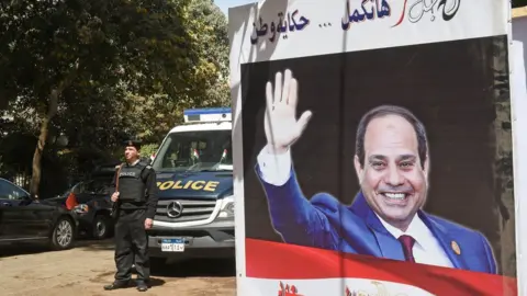 Getty Images Egyptian policemen standing next to an electoral banner depicting President Abdel Fattah al-Sisi in the capital Cairo. March 26, 2018
