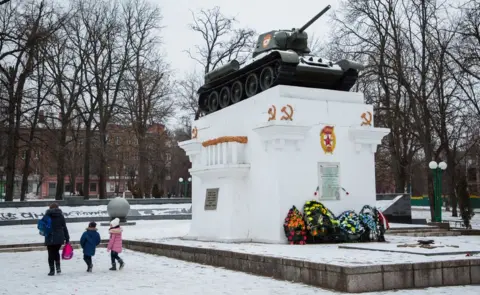 BBC A mother and her two children walk past a Soviet world war two memorial in snowy Kamyanets-Podilskyi