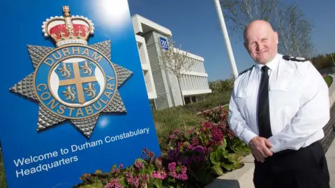 Durham Constabulary Mike Barton stands next to a Durham Constabulary logo
