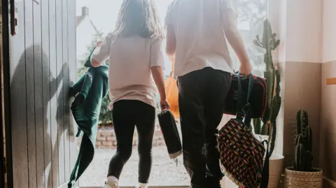 Getty Images Children leaving the front door in school uniform, carrying bags 