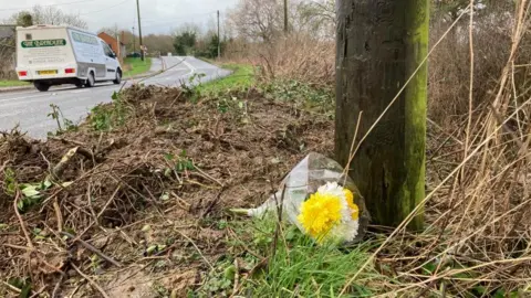 Section of verge where mud has been recently disturbed, with a small bouquet of flowers laid on the surface