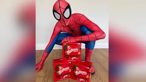 Spiderman wearing his suit crouched in front of Easter Egg boxes