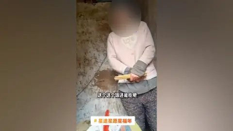 DOUYIN A screenshot of the video shows the woman with a chain around her neck standing in the hut