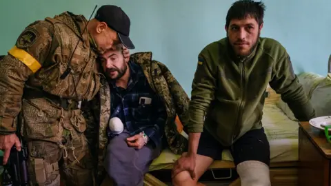 Getty Images Ukrainian service personnel visit their comrades Vitaly, who lost his hand, and Pasha, who wounded his knee, as they recover in a local hospital in Brovary 10 March 2022.