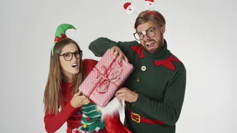 gpointstudio Two people dressed in Christmas clothes fighting over a Christmas present