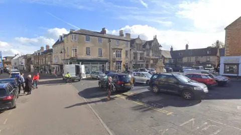 Google A view of Uppingham market place, which is full of parked cars while the sun shines.