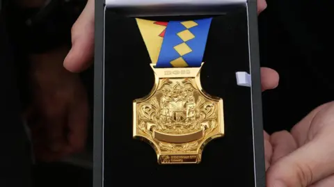 A highly-detailed gold cross-shaped medal on a multi-coloured ribbon in a black case